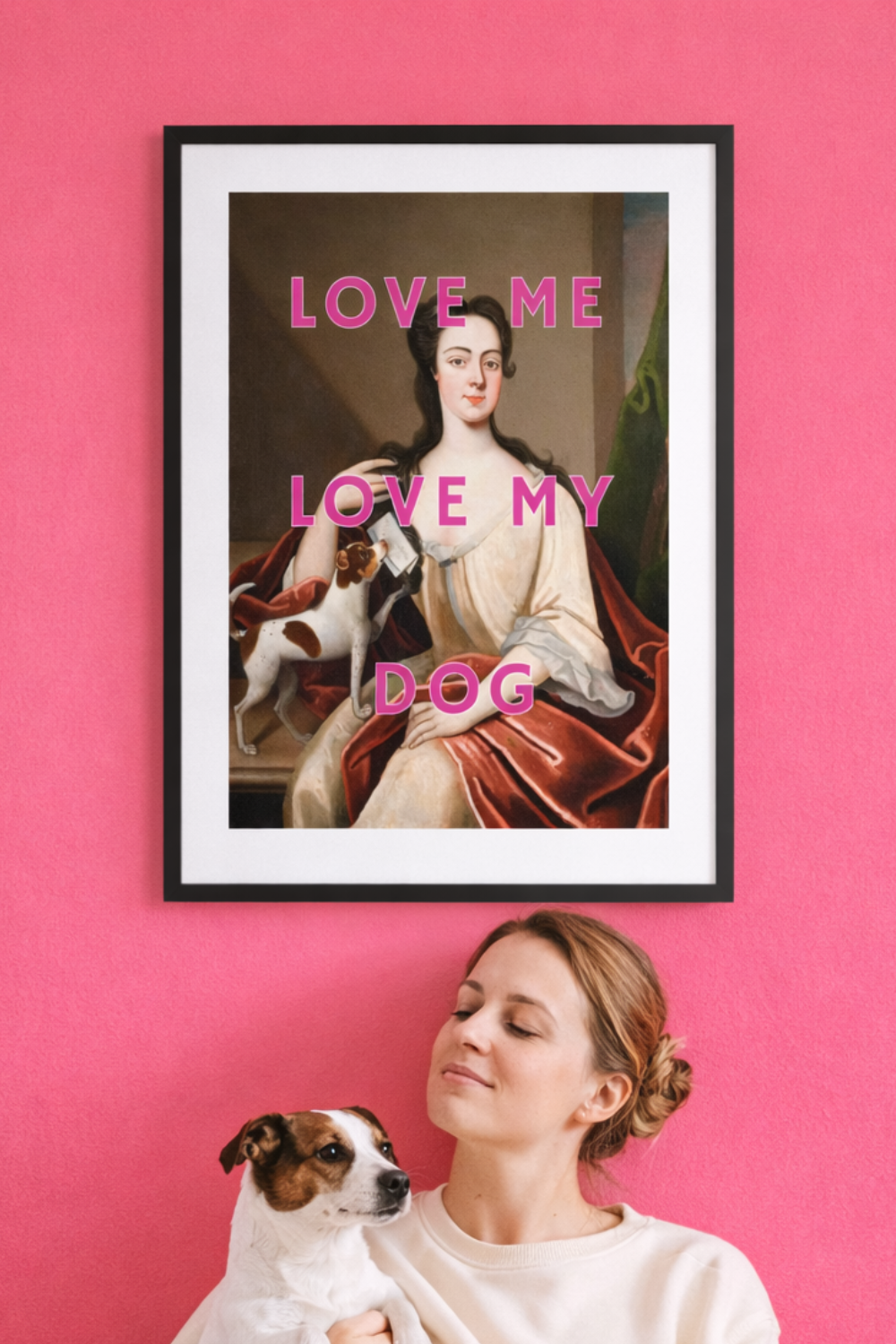 Altered classical art print reading “Love Me Love My Dog” styled in a pink interior with a woman holding her dog