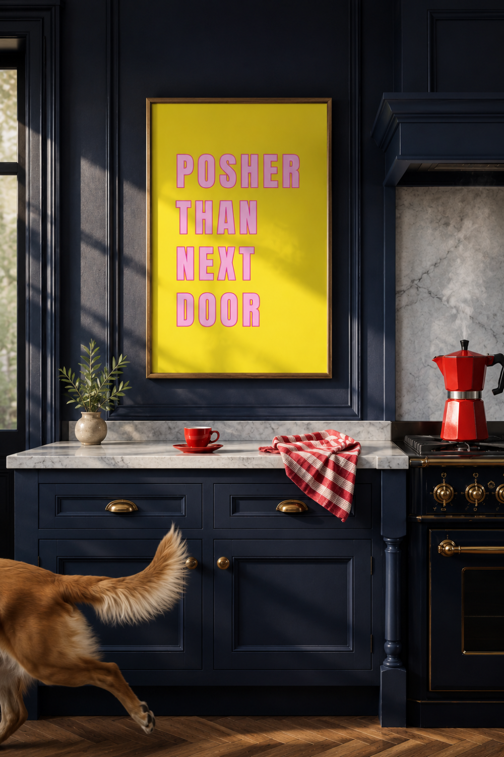 A framed art print featuring the text 'POSHER THAN NEXT DOOR' in pink on a bright yellow background, displayed on a dark navy kitchen wall above a marble countertop with a red moka pot and a dog walking in the foreground.